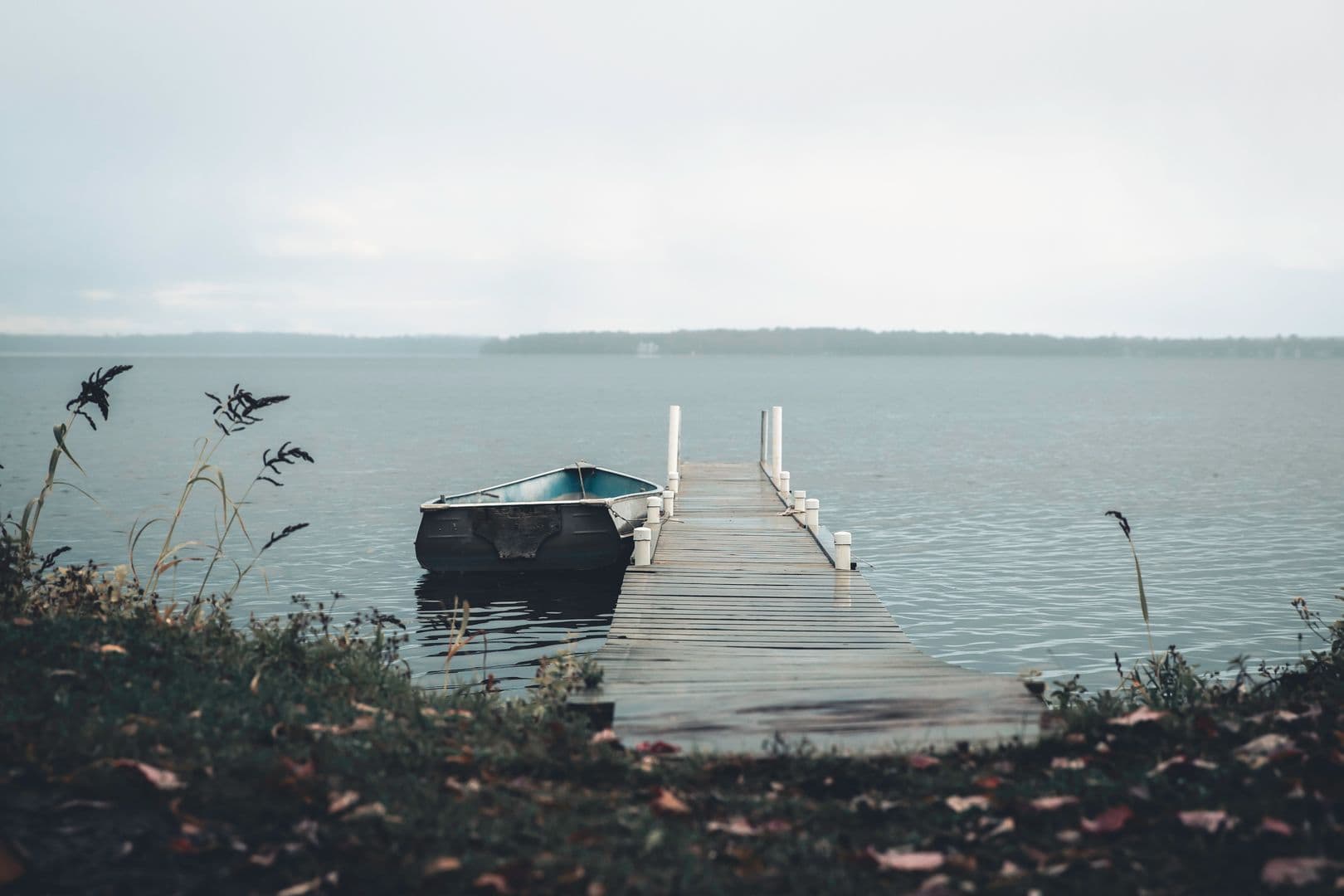 A small boat moored at a quiet wooden dock on a calm, overcast lake