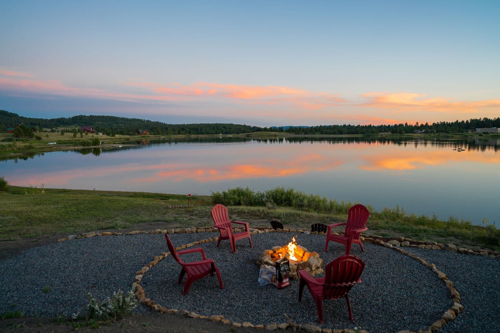 Empty chairs around a lakeshore campfire burning at dusk
