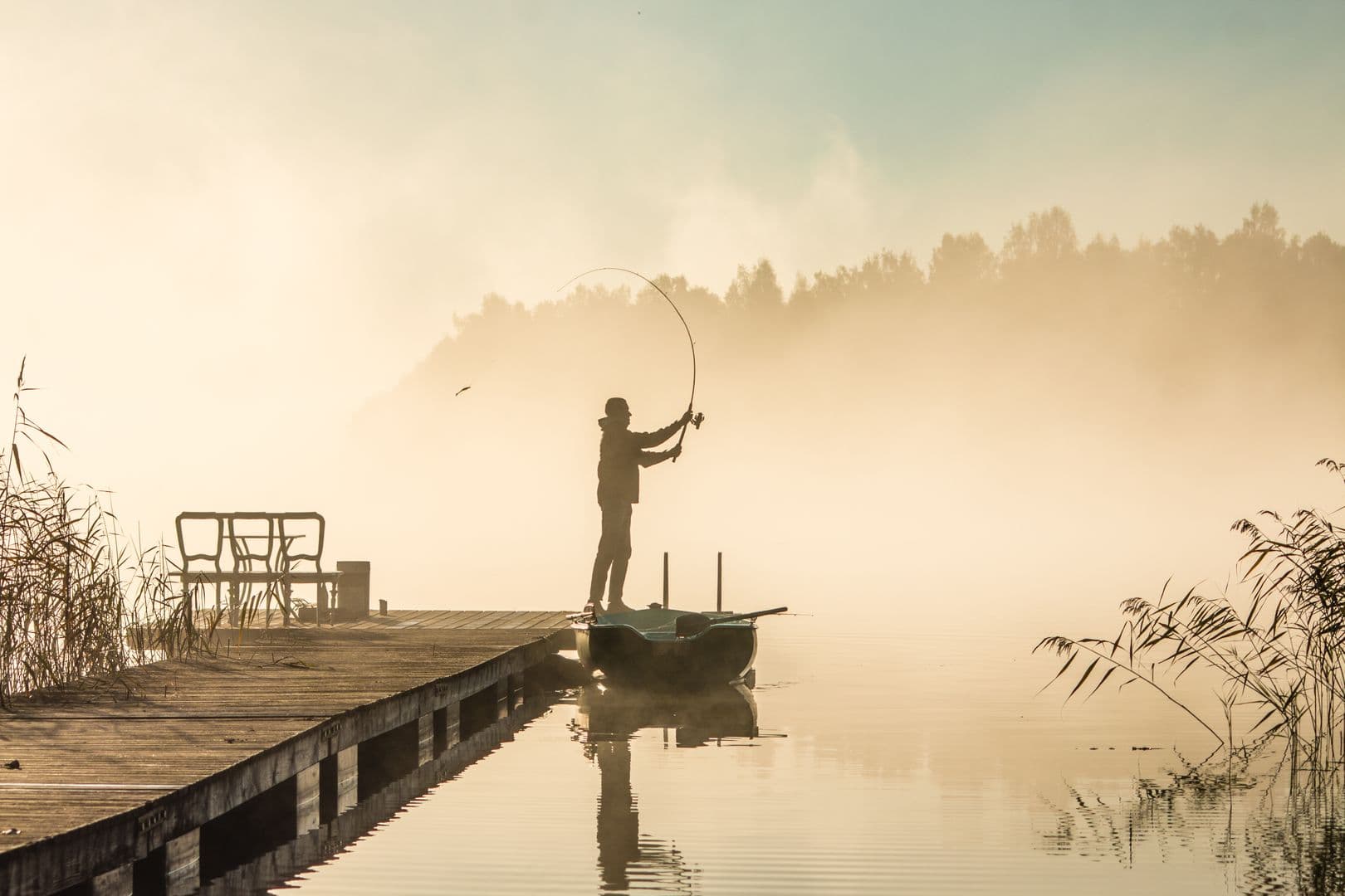 A lone angler casting a line from a dock on a misty lake at sunrise